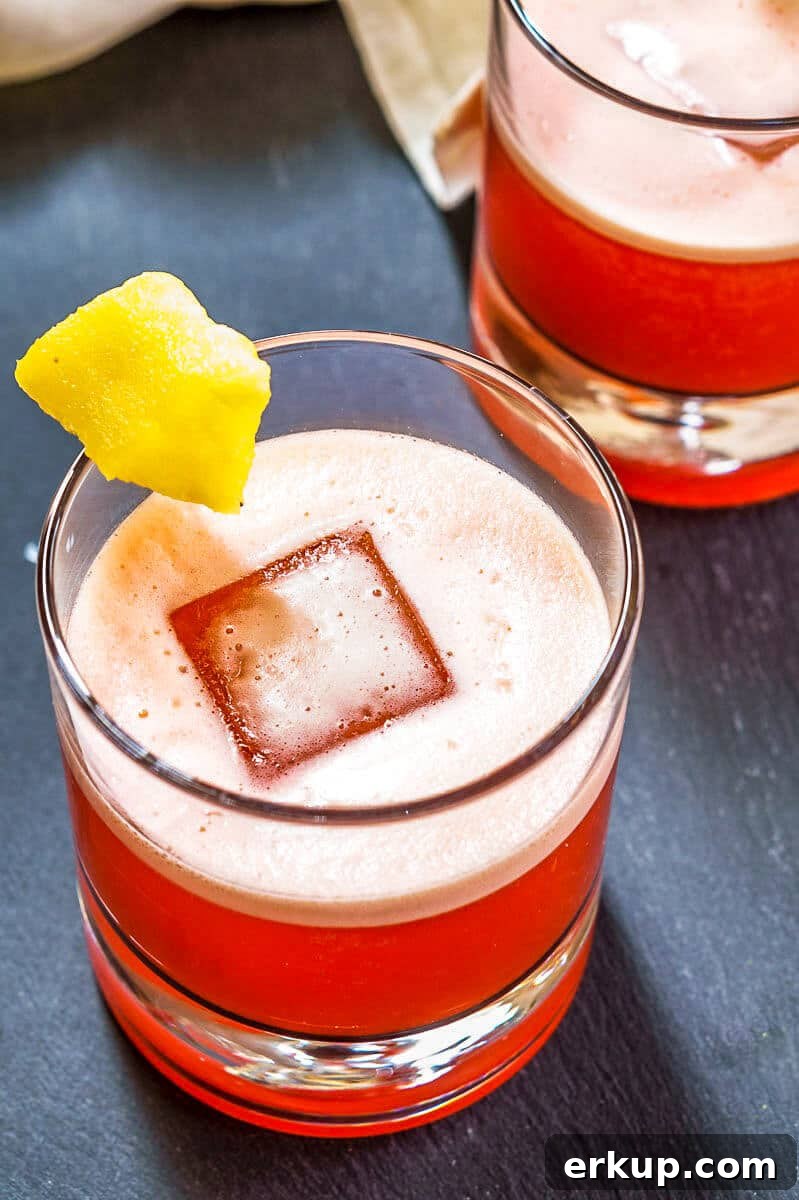 Top down view of a rocks glass filled with a red foam-topped Campari Cocktail garnished with a piece of pineapple.