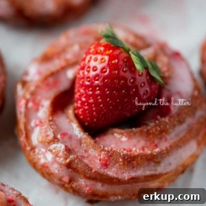Strawberry glazed french crullers on a parchment paper lined baking sheet topped with a fresh strawberry.