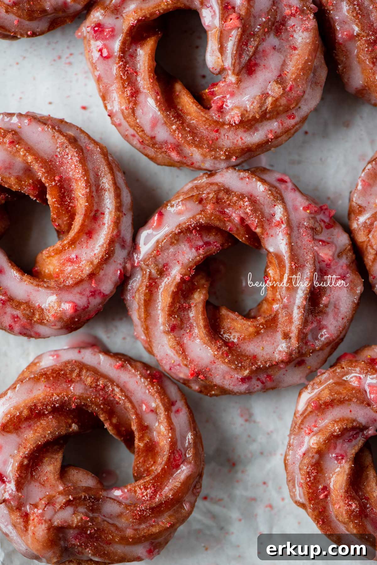 Strawberry glazed french crullers sprinkled with strawberry sugar on a parchment paper lined baking sheet
