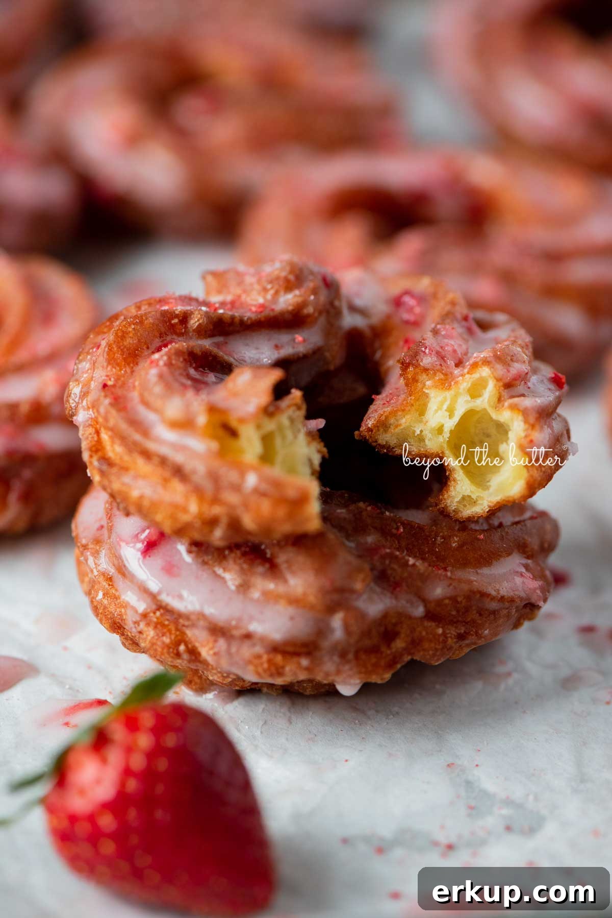 Light and airy stacked strawberry glazed french crullers with bite taken out of the top cruller