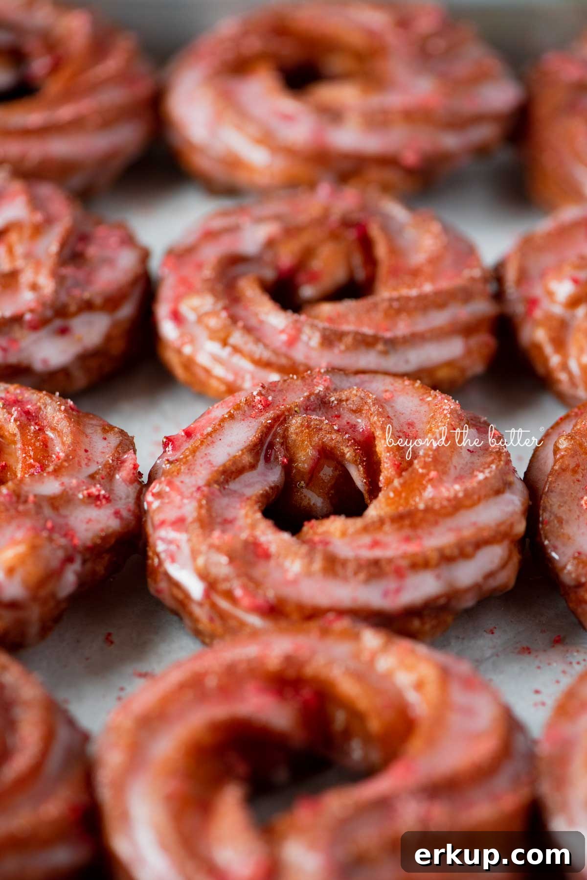 Strawberry glazed french crullers sprinkled with strawberry sugar on a parchment paper lined baking sheet
