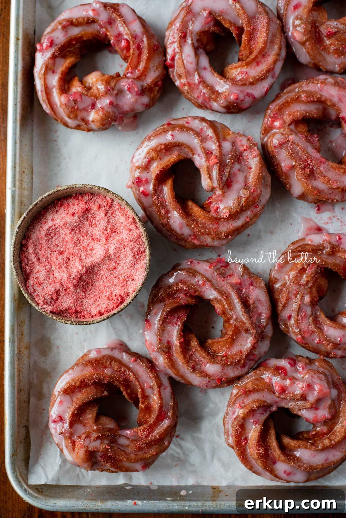 Strawberry glazed french crullers sprinkled with strawberry sugar on a parchment paper lined baking sheet