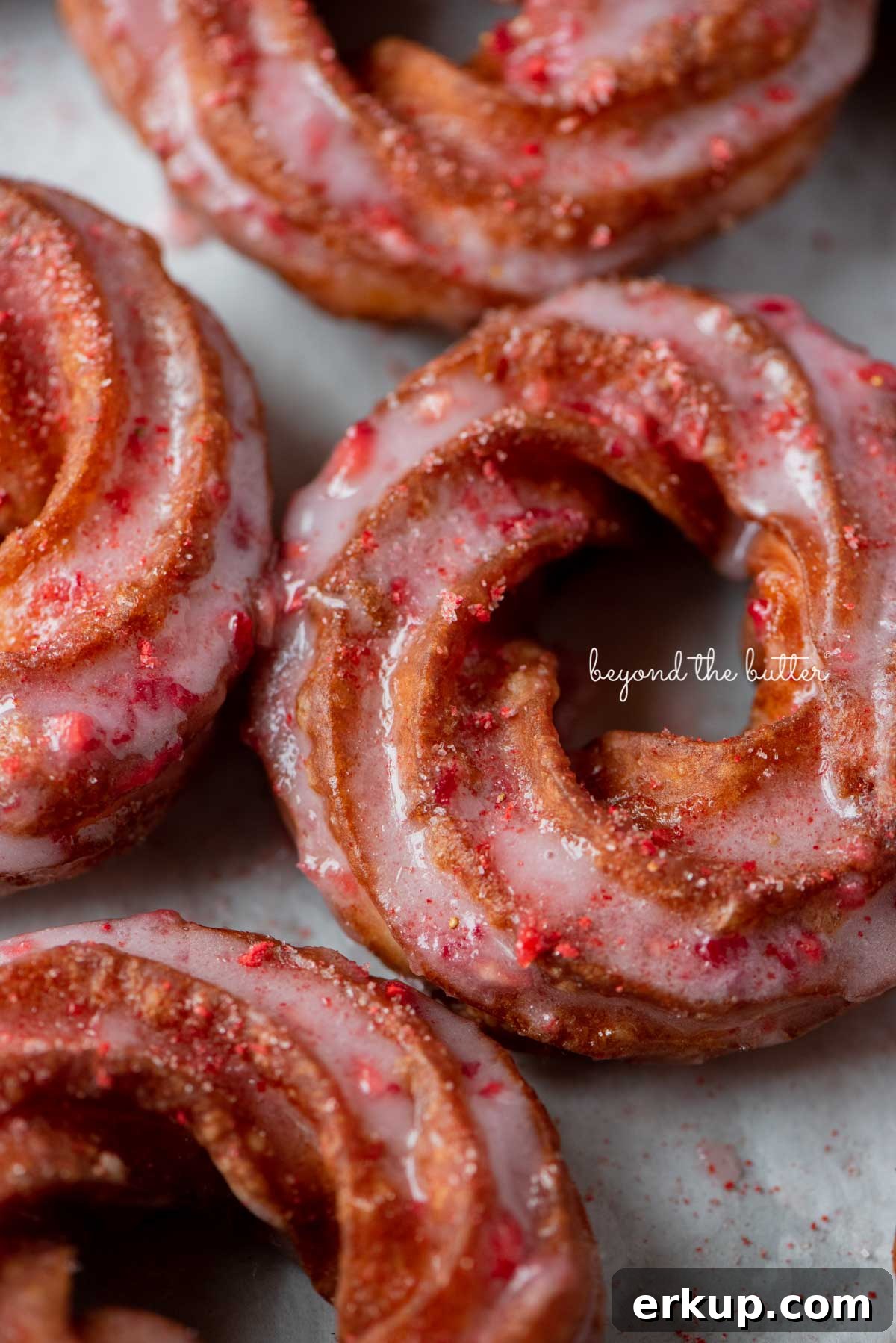 Strawberry glazed french crullers sprinkled with strawberry sugar on a parchment paper lined baking sheet
