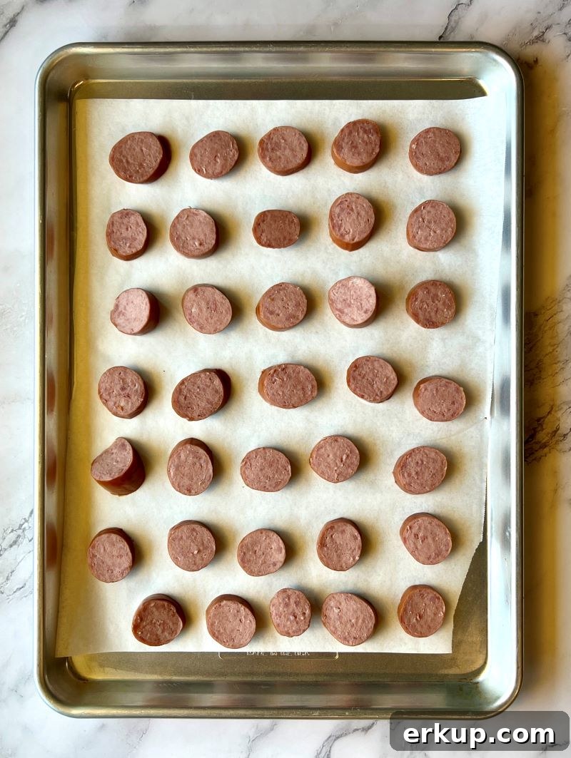 Uncooked smoked sausage slices on a sheet pan lined with parchment paper.