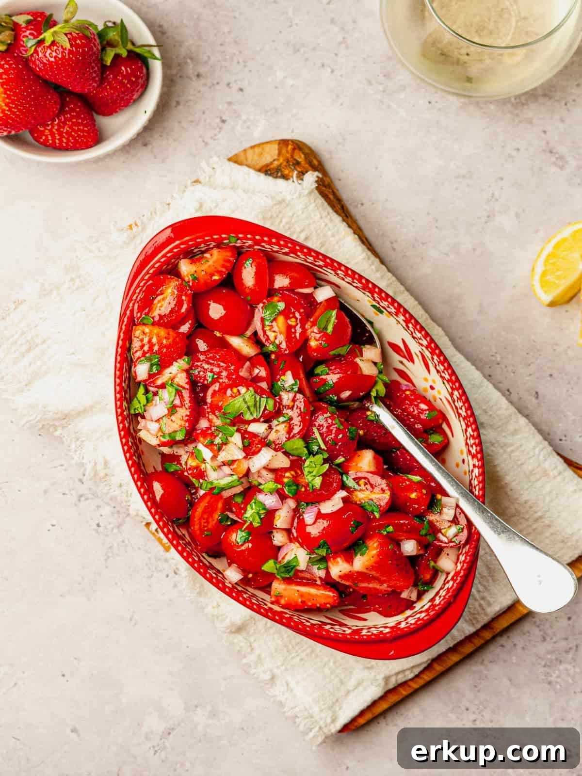 A bowl filled with strawberries and tomatoes on a napkin lined cutting board.