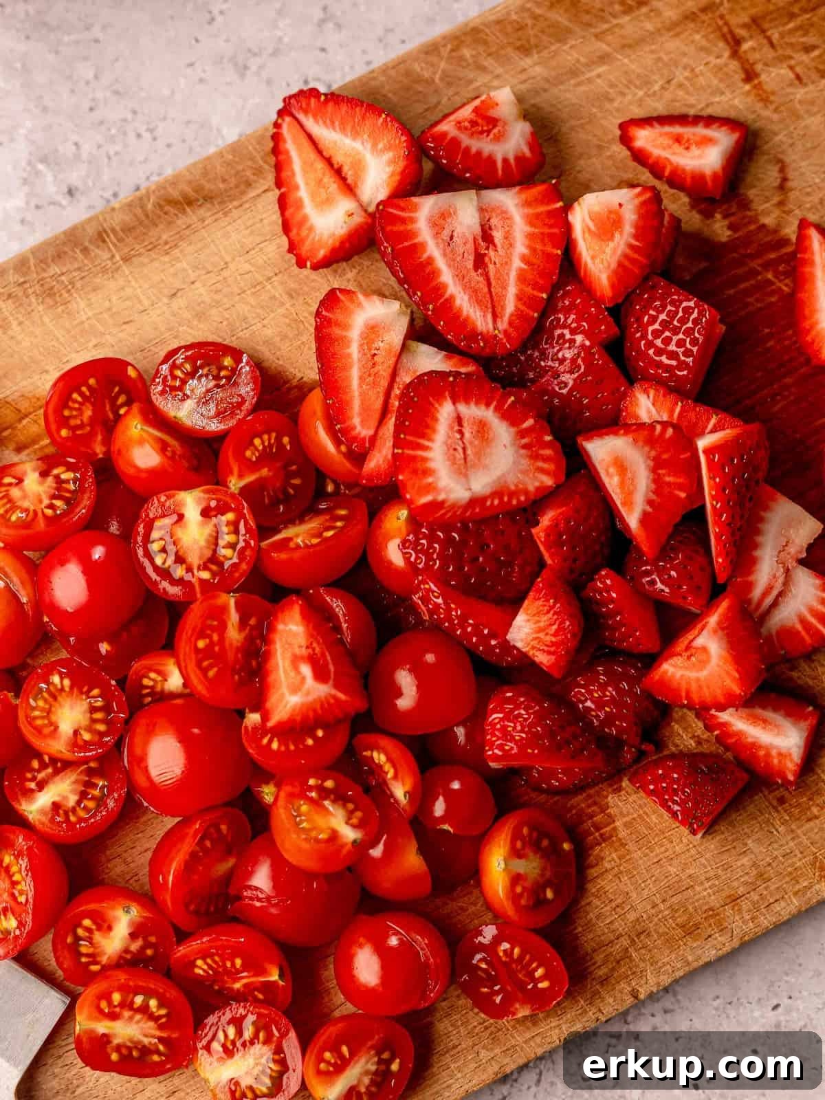 Chopped tomatoes and strawberries on a cutting board.