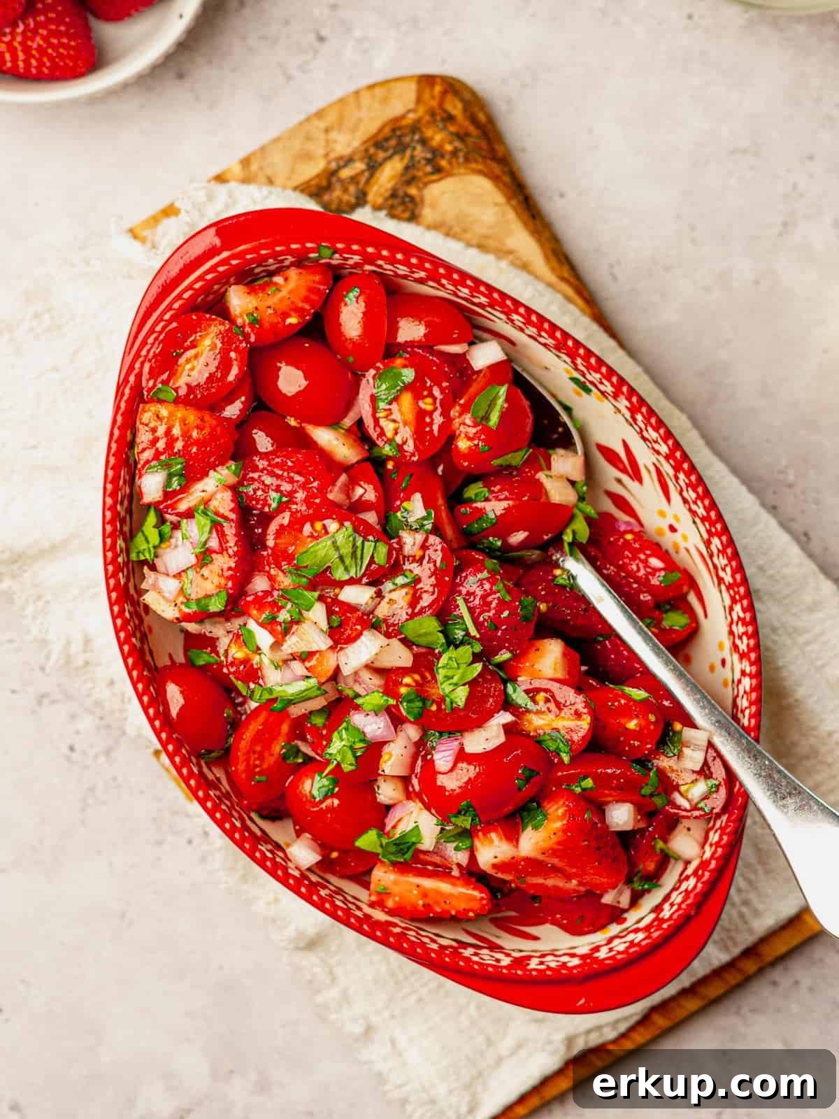 Bowl filled with strawberries and tomatoes with a serving spoon.