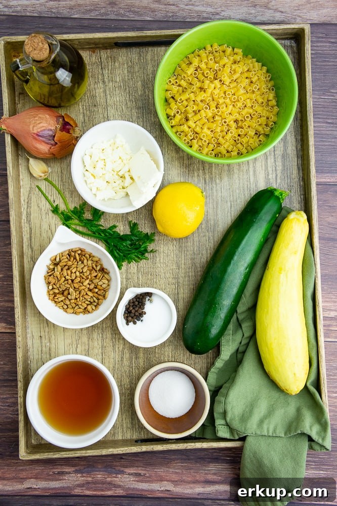 a serving tray with two summer squash, a bowl of uncooked pasta, a lemon, parsley, a shallot, olive oil, apple cider vinegar, and salt and pepper