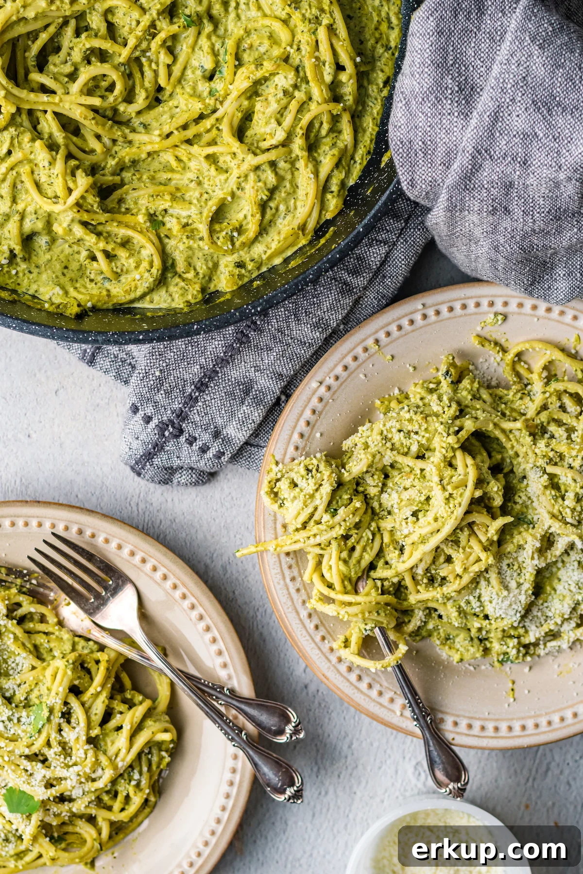 Overhead look at two dinner plates with green mexican spaghetti next to a pan full of it.