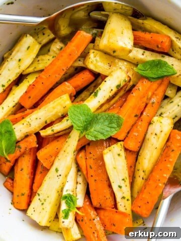 A bowl of roasted carrots and parsnips with serving spoons in it.