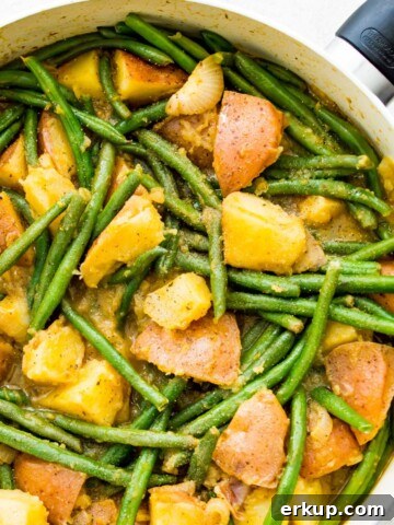 A pan filled with cooked green beans and potatoes.