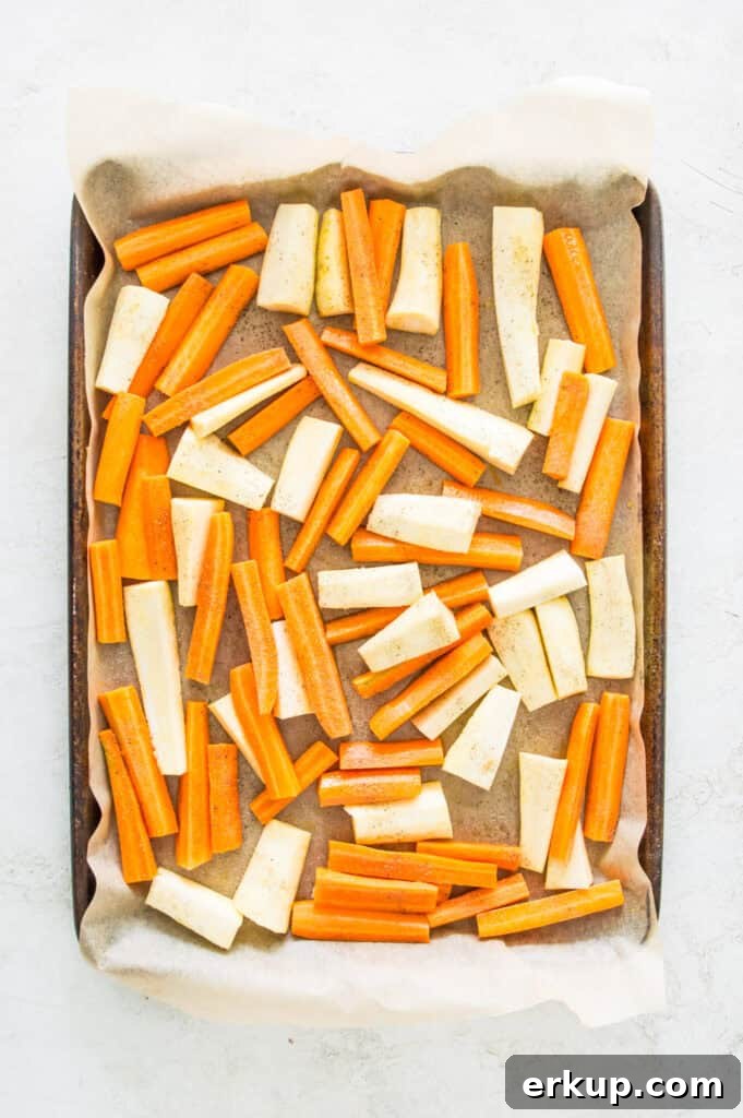 A baking sheet lined with parchment paper with peeled and chopped carrots and parsnips on it.