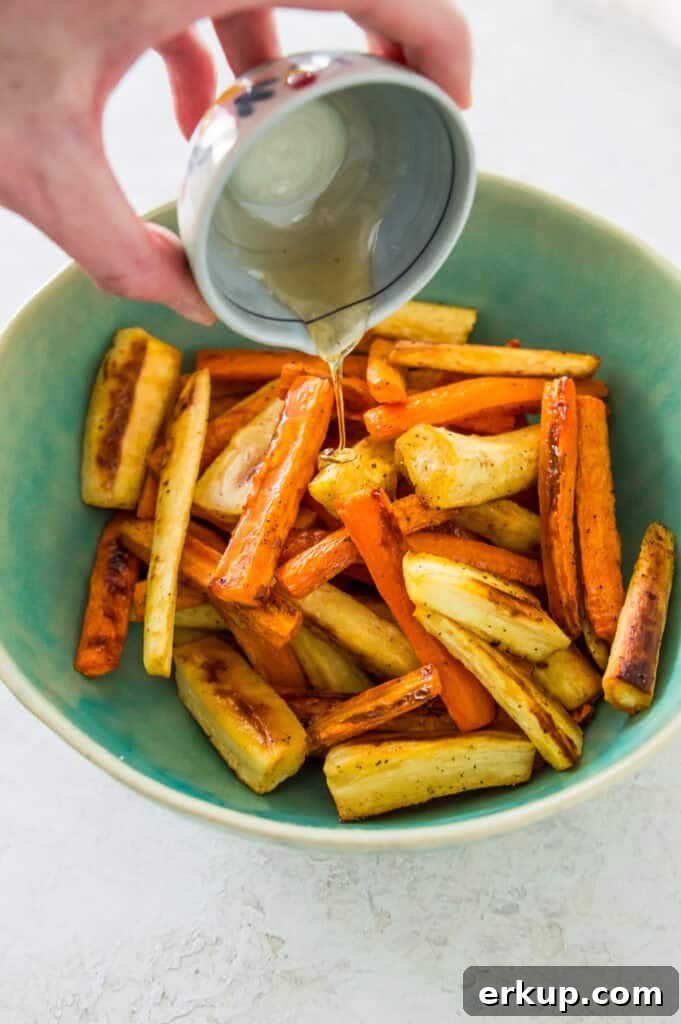 A honey glaze being poured over a bowl filled with roasted carrots and parsnips.