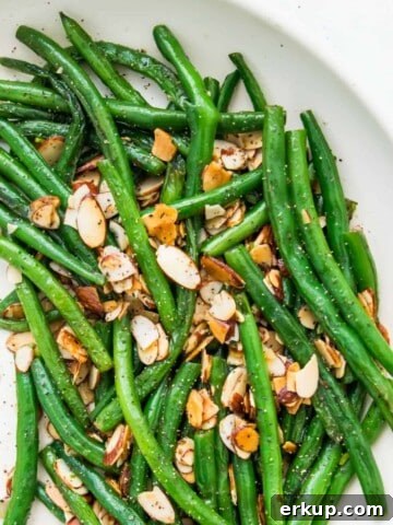 A plate of cooked green beans topped with roasted slivered almonds.