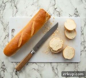 overhead shot of french bread being sliced on plastic chopping board with bread knife