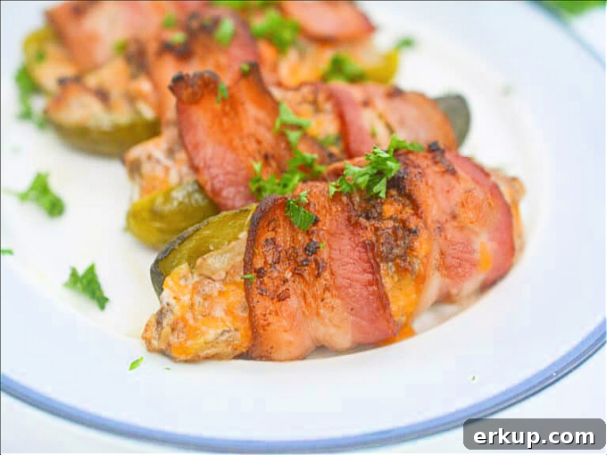 Keto Bacon-Wrapped Cheeseburger Pickle Poppers Recipe 2 cheeseburger inside pickle wrapped in bacon on white plate.