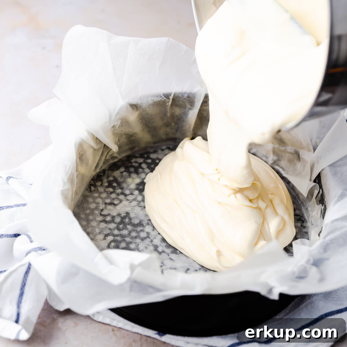 cheesecake batter being poured into baking tin lined with baking paper.