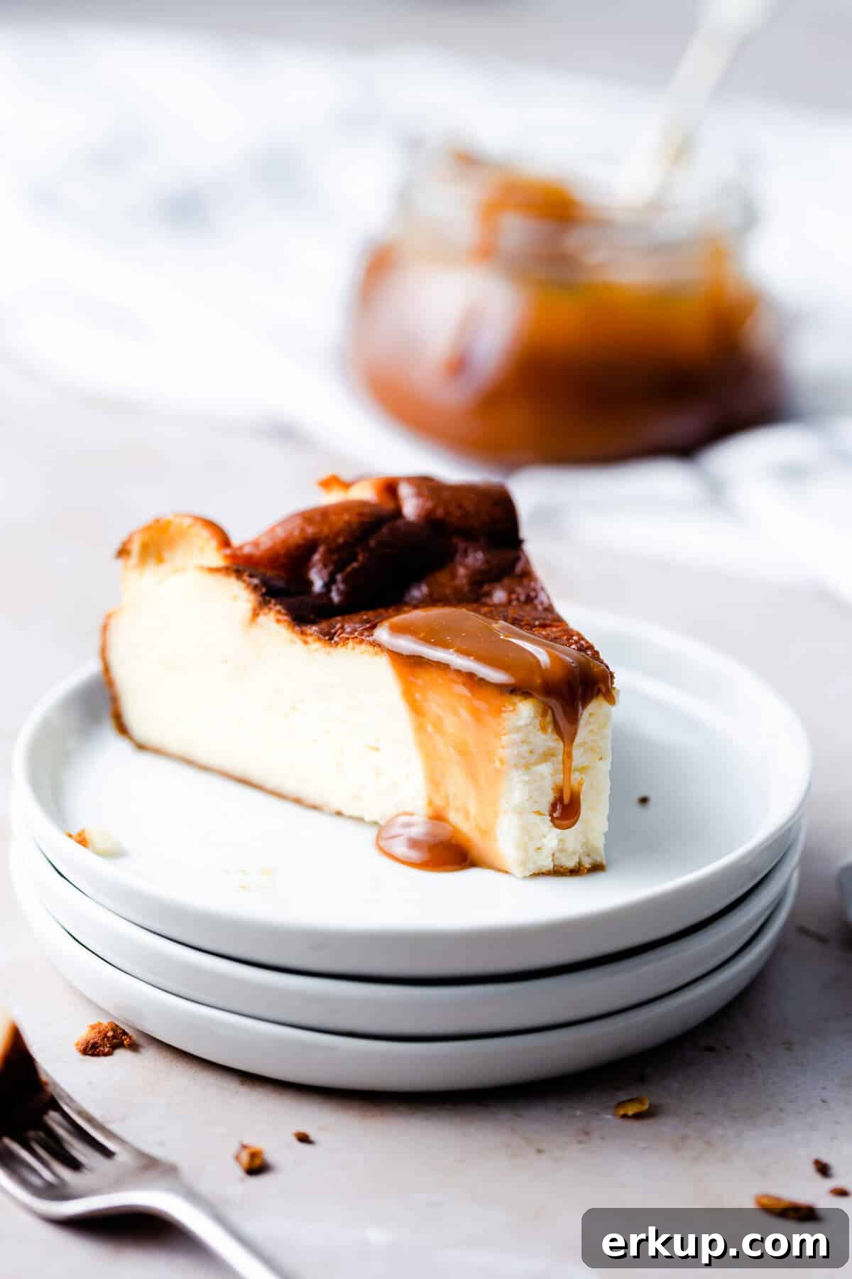 side angle close up at a slice of burnt cheesecake with a bite missing and some caramel sauce dripping from top