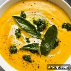 Creamy roasted pumpkin soup with pesto and garnished sage leaves in a white bowl.
