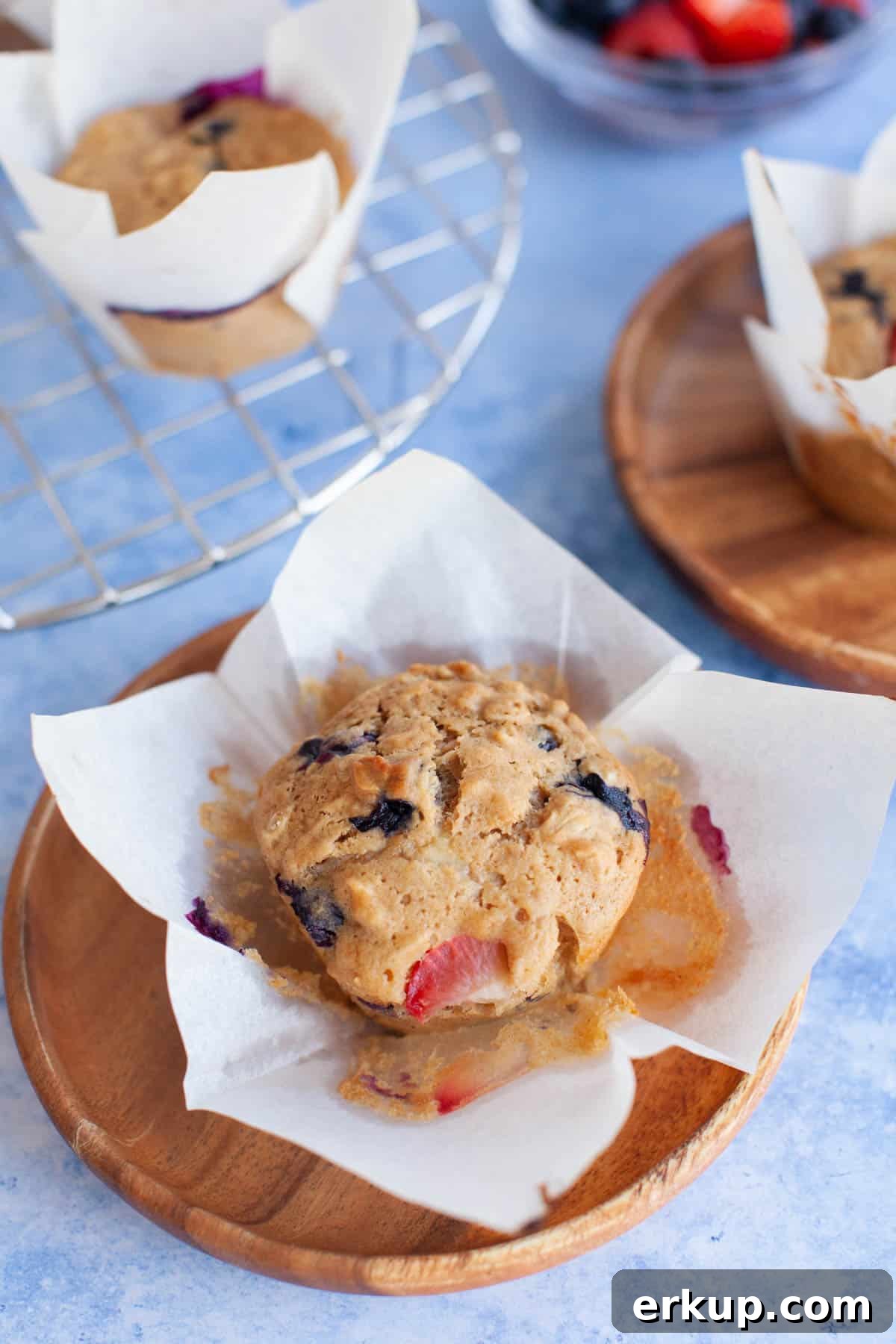 Mixed Berry Muffins Recipe: Moist Blueberry Raspberry Muffins 2 ready to eat berry muffins on wood plates next to a cooling rack of muffins.