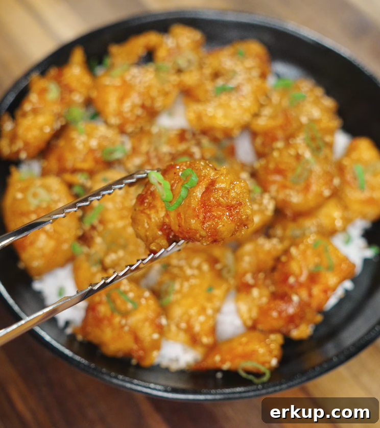 Hot Honey Butter Chicken Recipe 3 A piece of saucy sriracha honey chicken held above a bowl of rice using tongs