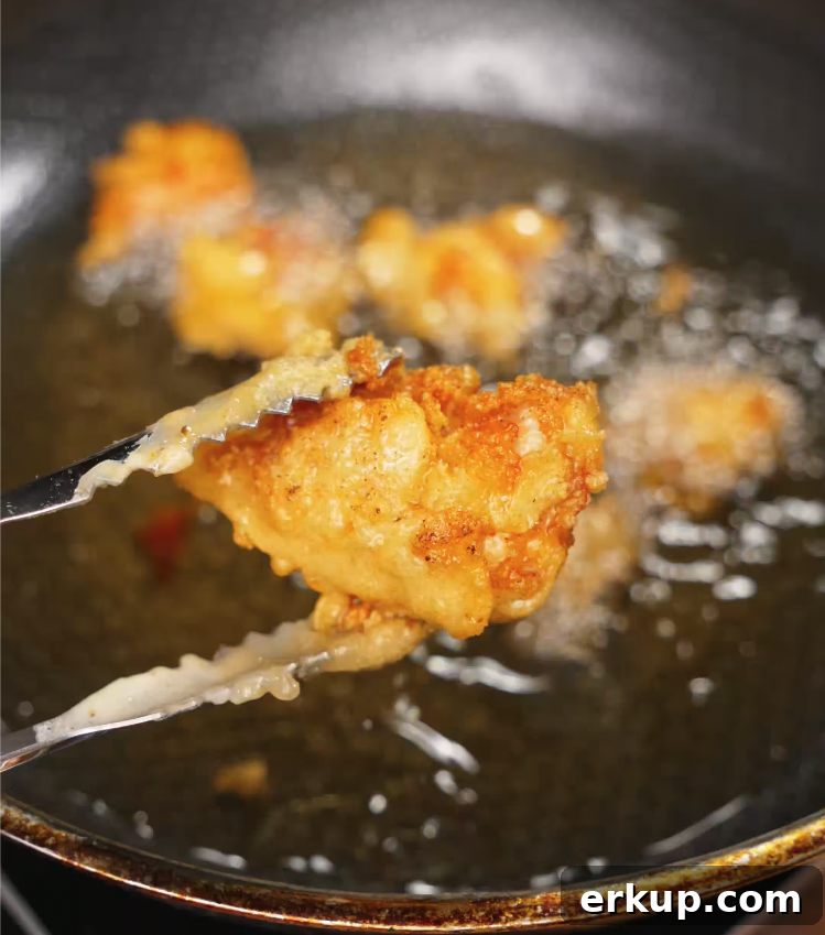 Hot Honey Butter Chicken Recipe 6 Tongs lifting crispy golden fried chicken out of hot oil during deep frying