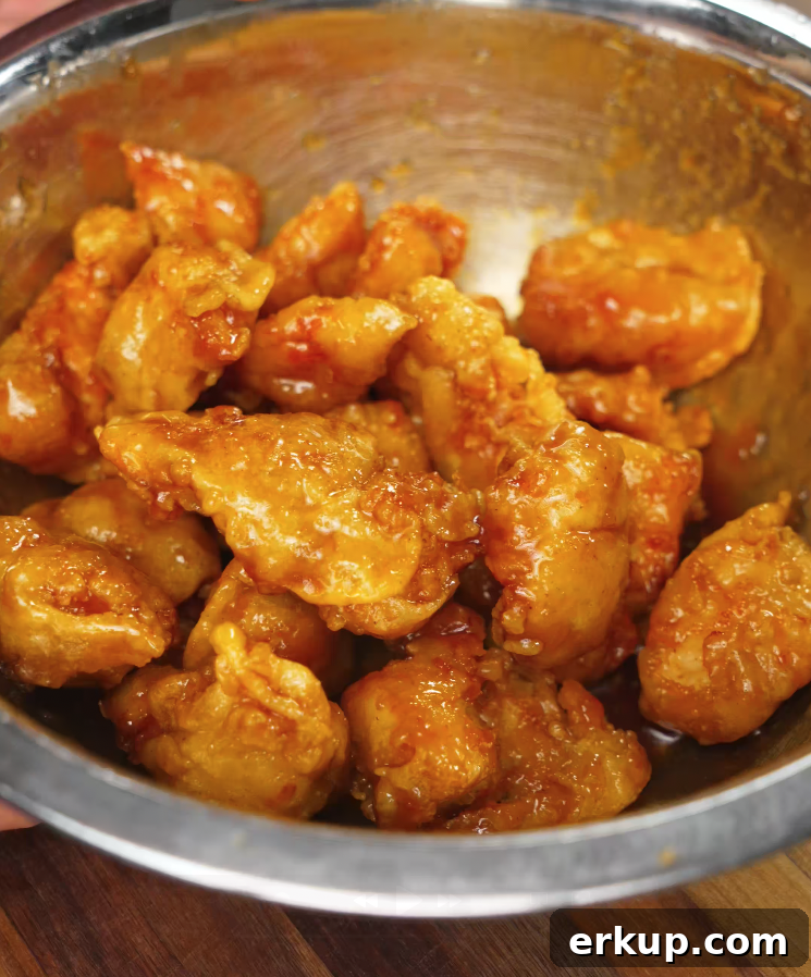 Hot Honey Butter Chicken Recipe 7 Golden fried chicken being coated in sticky sriracha honey butter sauce in a metal bowl