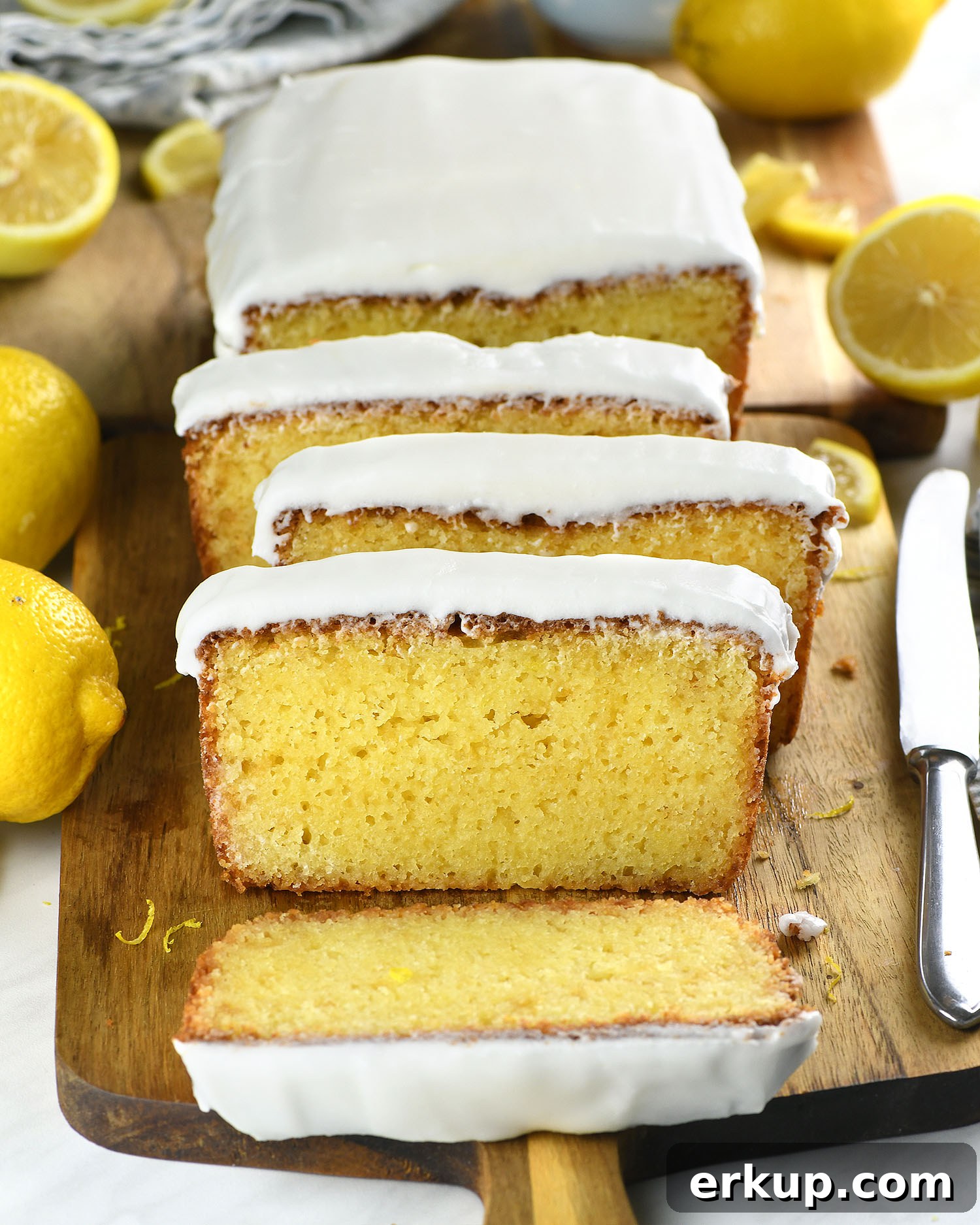 Sliced lemon pound cake with thick lemon glaze on a wooden board with fresh lemons.