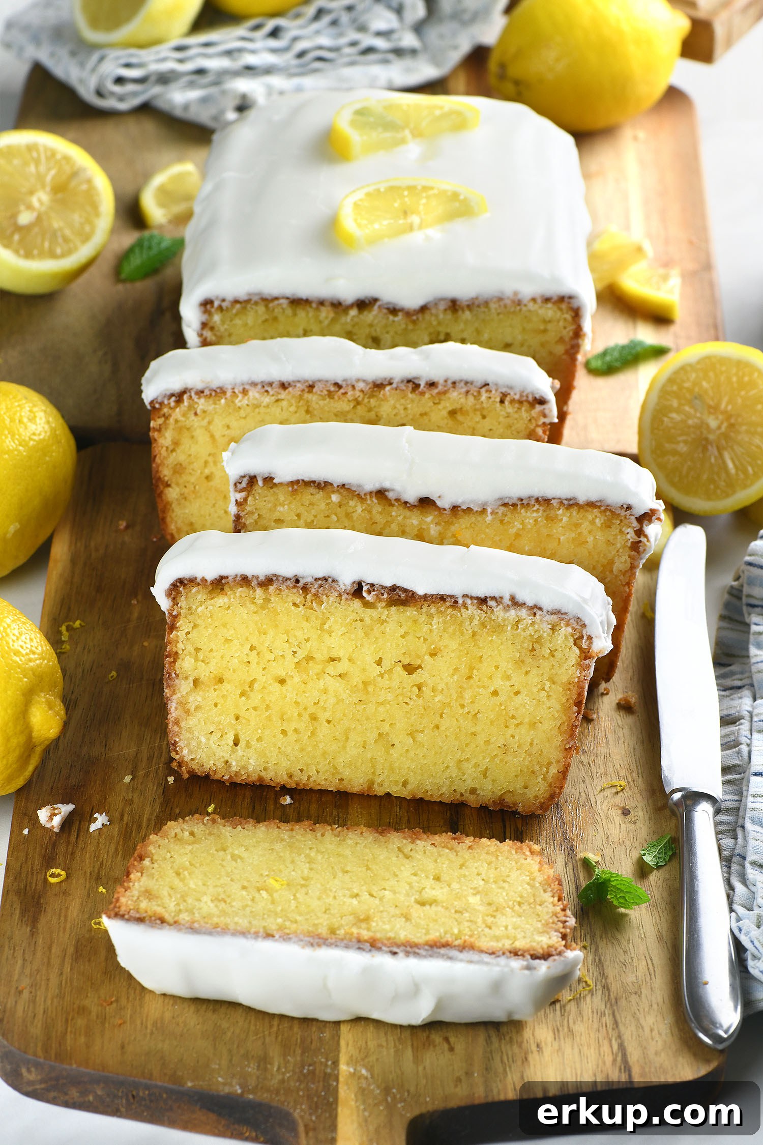 Moist lemon pound cake slices with thick lemon glaze on a wooden board with fresh lemons.