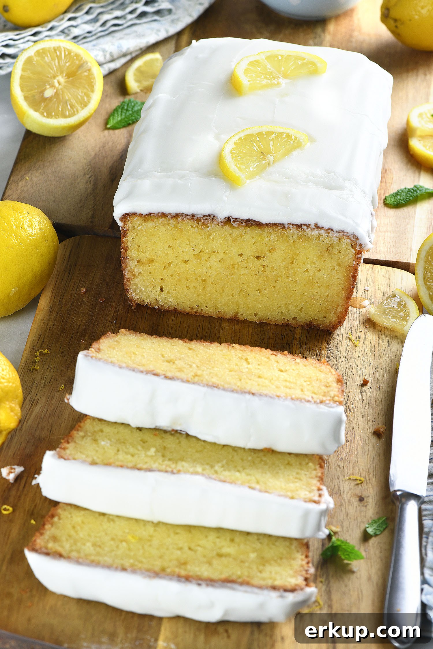 Lemon pound cake with thick white glaze and lemon slices, served with sliced cake on a wooden board.