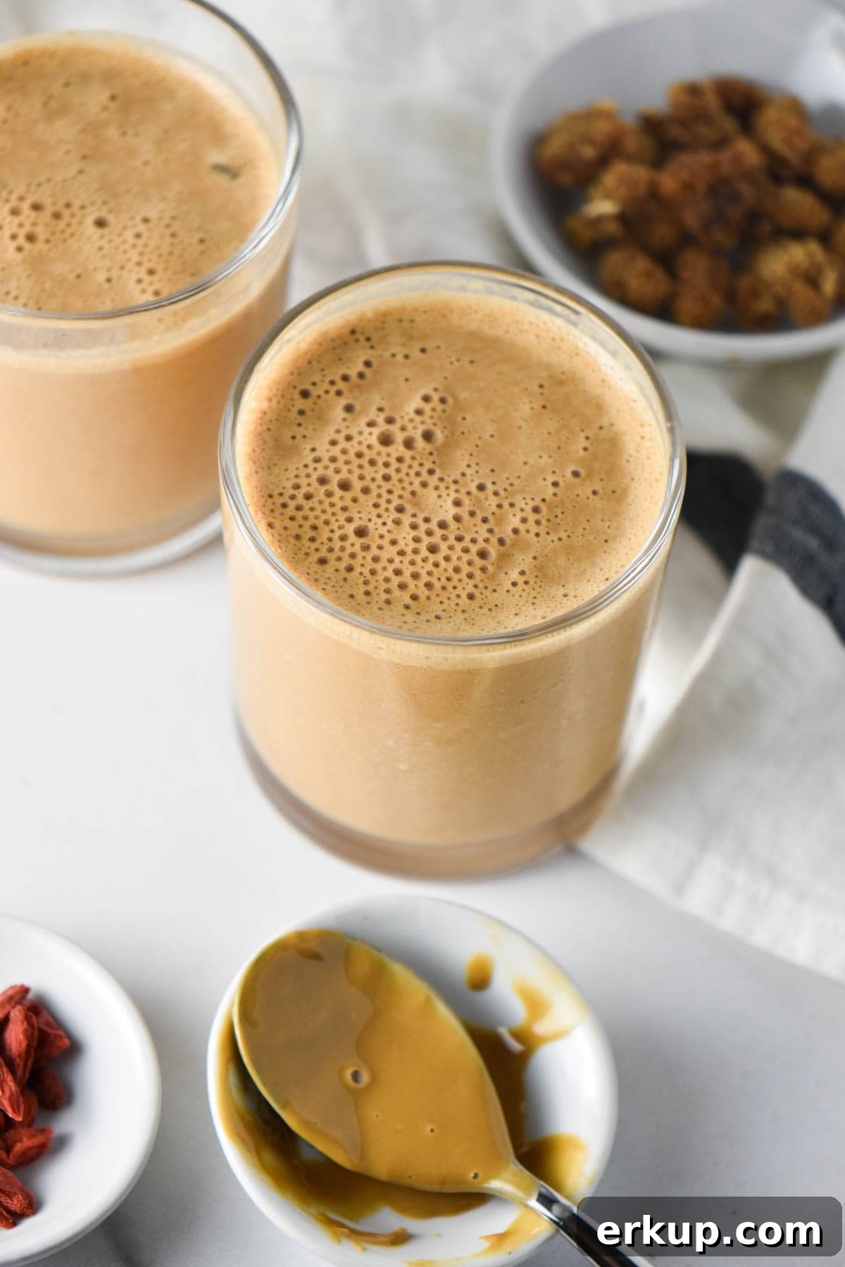 Creamy Sunflower Seed Butter and Maca Smoothie Recipe 6 A jar of mulberries next to two smoothie glasses and sunbutter on a white table.