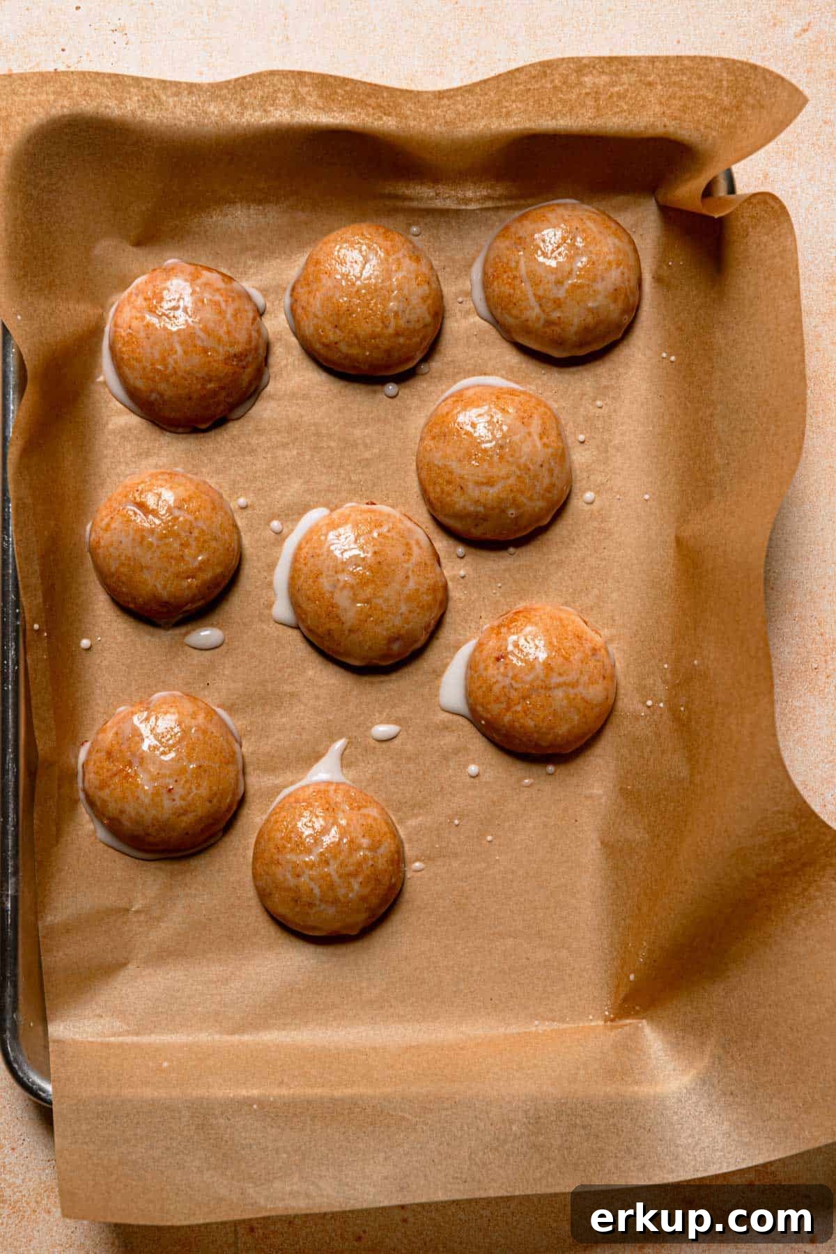 Glazed cookies over a cookie pan lined with parchment paper.