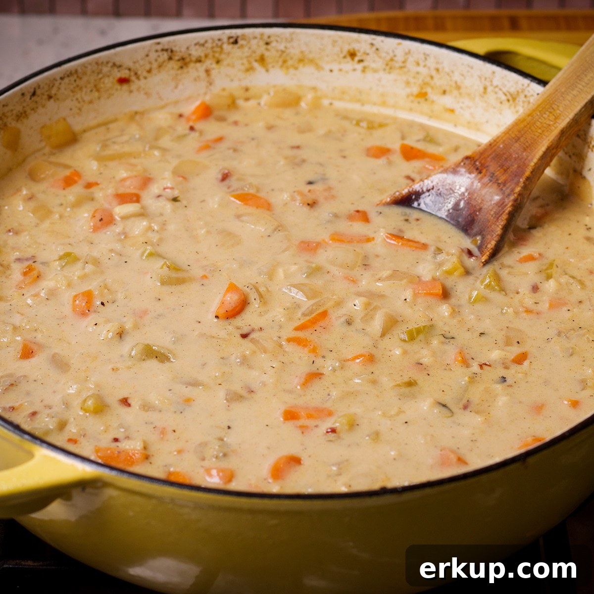 Using a wooden spoon to stir cream into simmering chicken and wild rice soup.