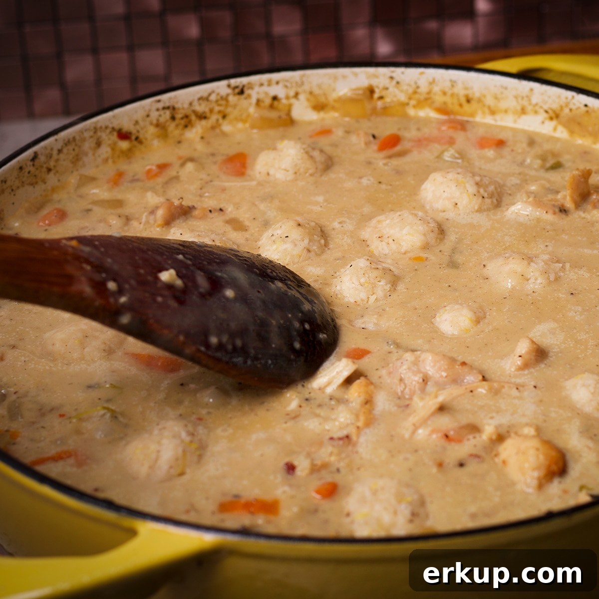 Using a wooden spoon to push parmesan dumplings down into simmering soup broth so they can cook.