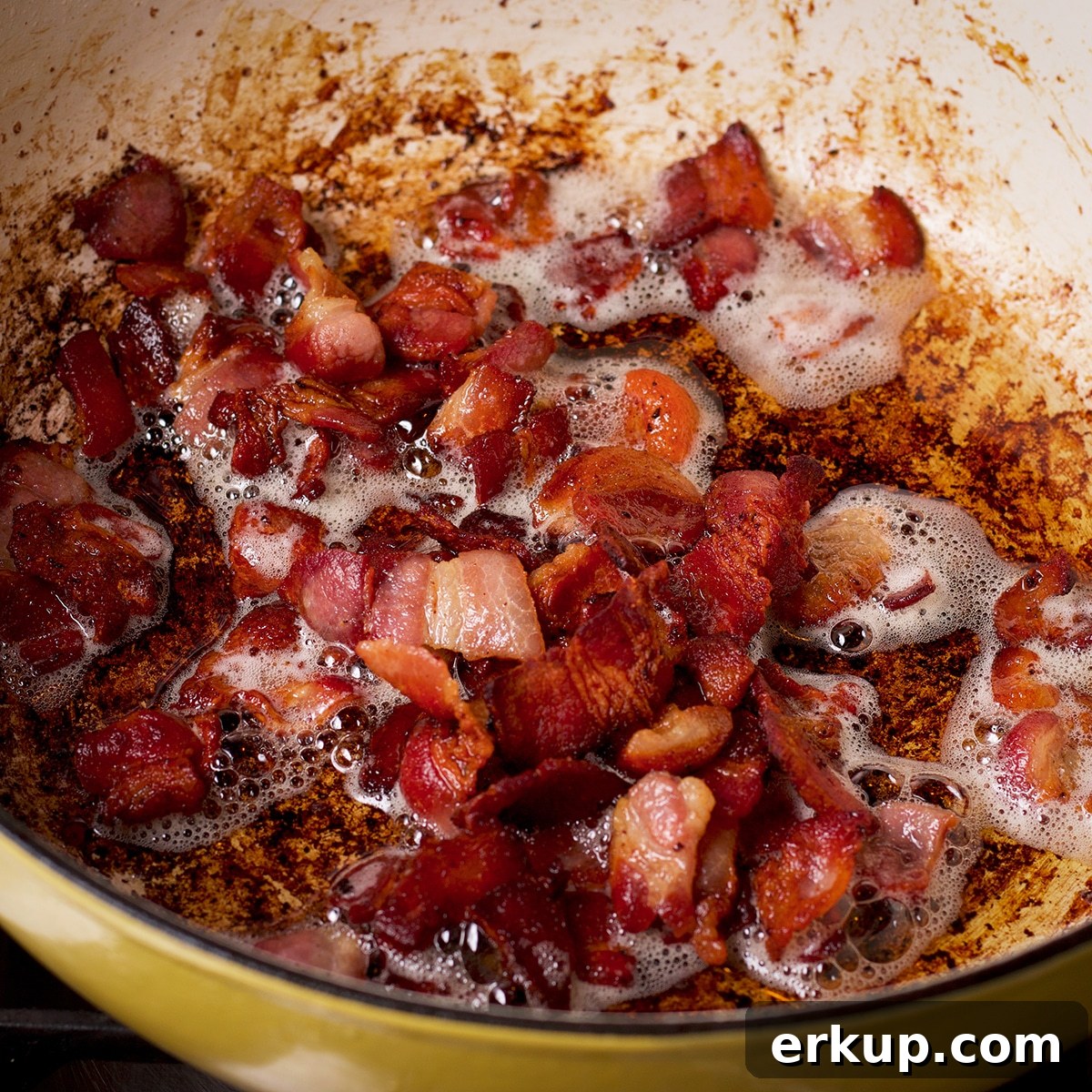 Chopped pieces of bacon cooking in a pan.
