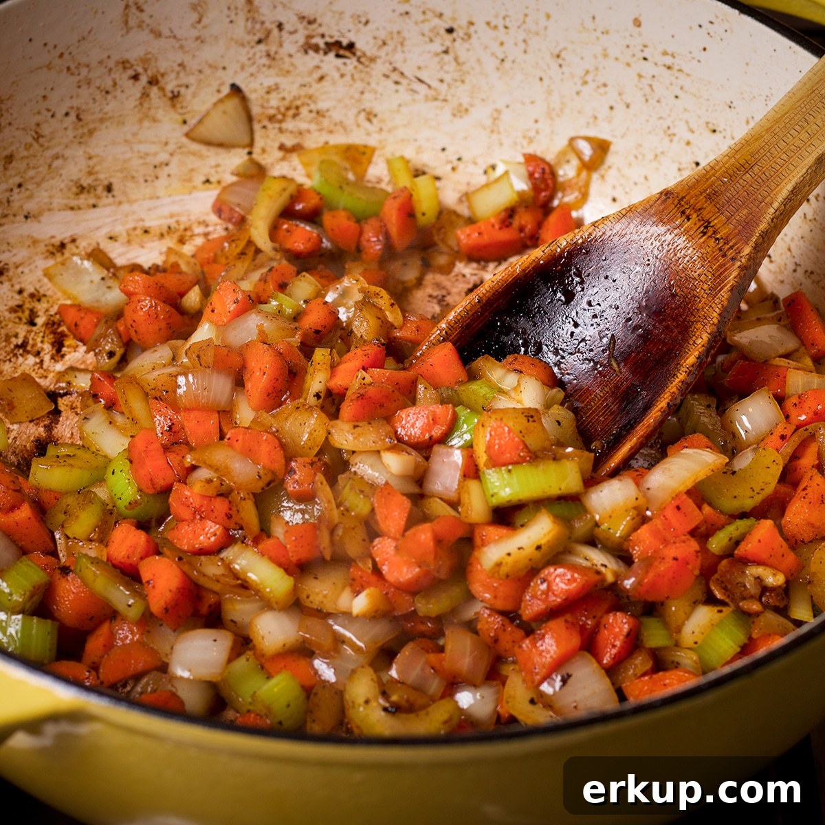 Using a wooden spoon to stir chopped vegetables as they cook in a pan.