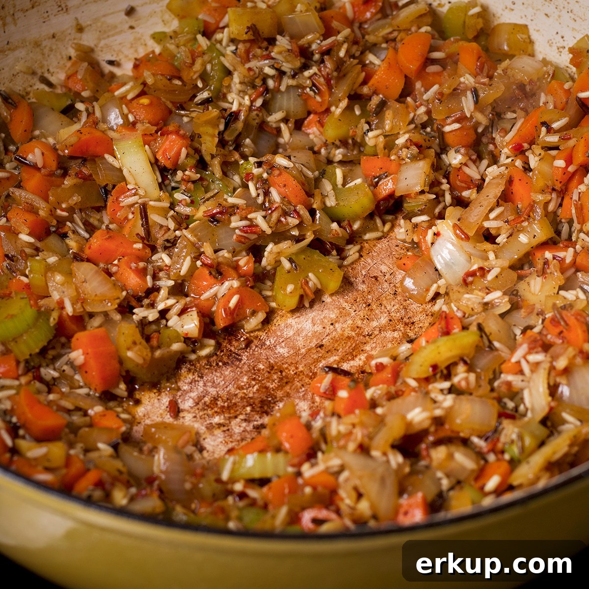 A pan filled with chopped vegetables and wild rice with white wine that was added but has now evaporated.