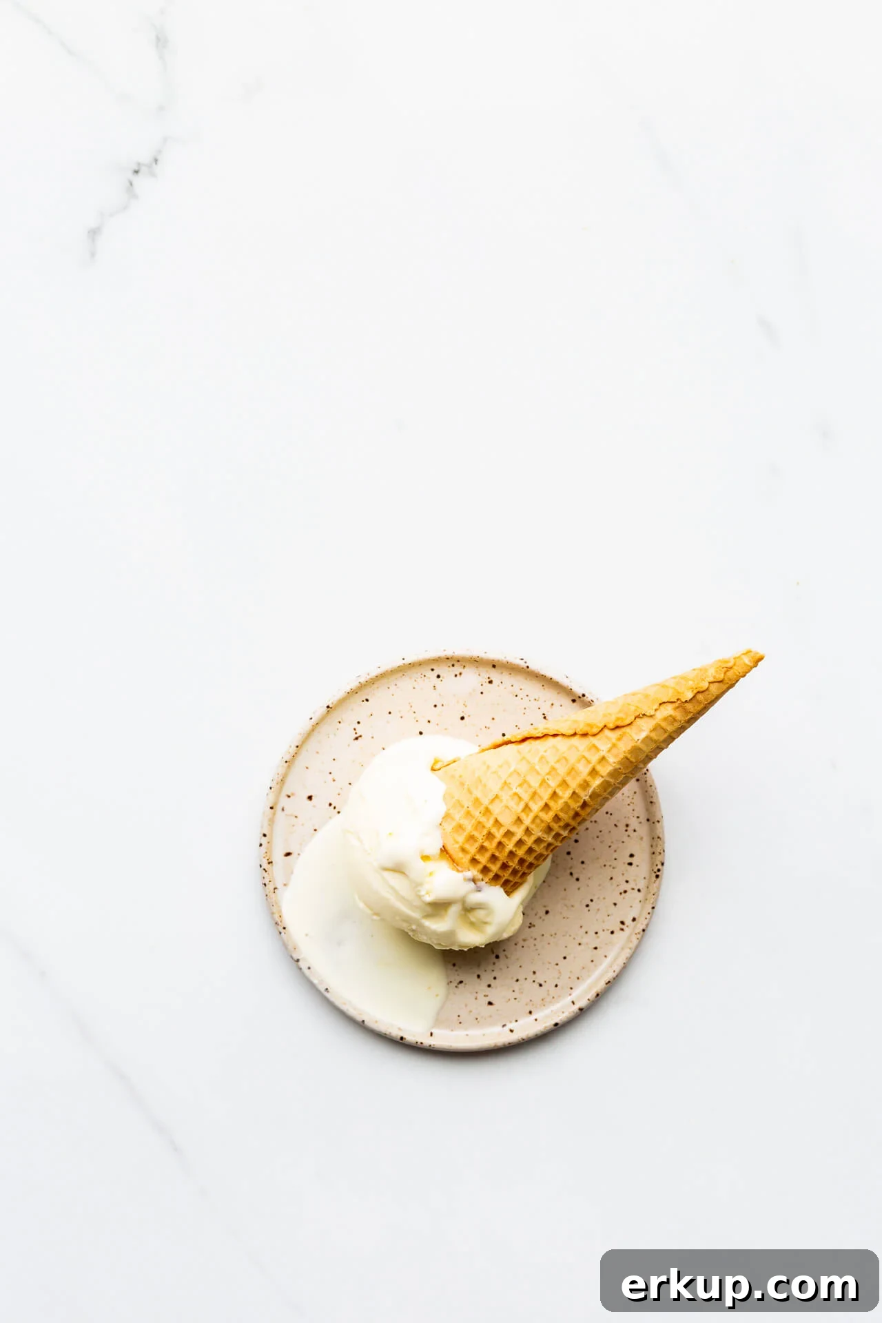 Lemon ice cream with cone on speckled plate, melting