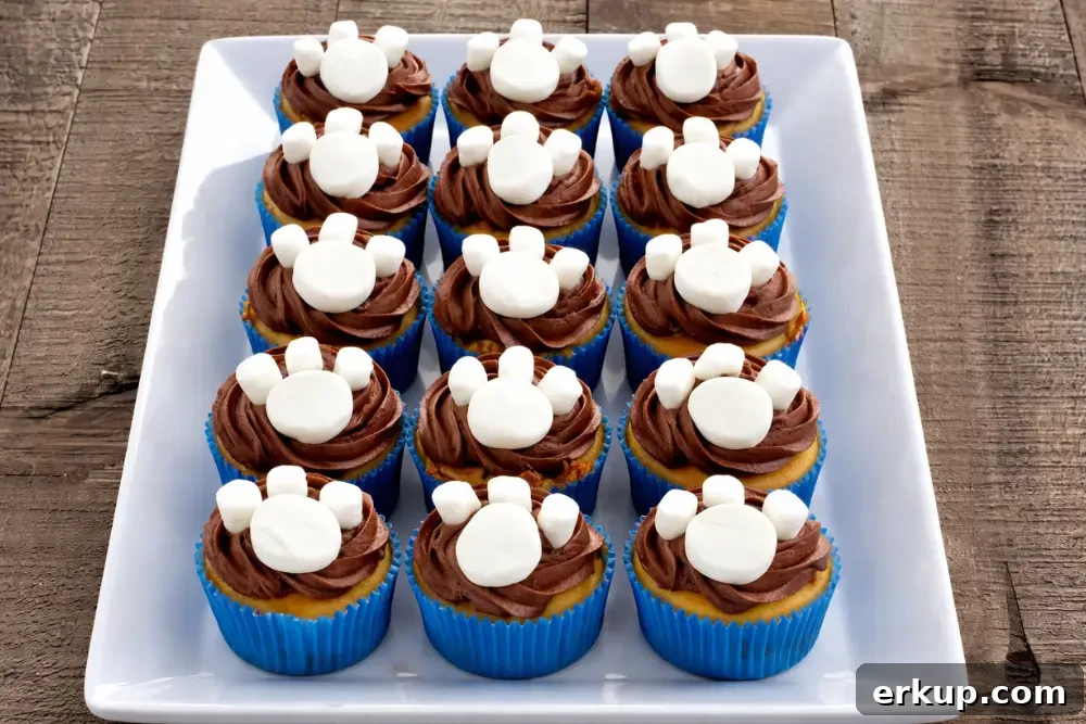 Paw patrol cupcakes topped with chocolate icing and marshmallow paw decorations on a tray.