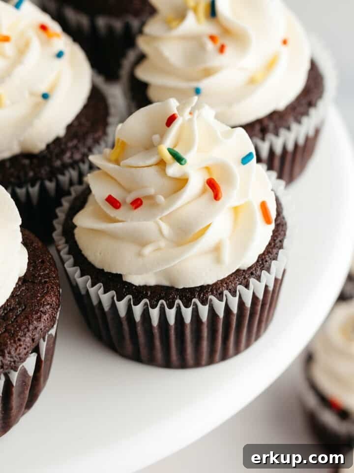 Chocolate cupcakes with a white frosting and rainbow sprinkles on a cake stand.