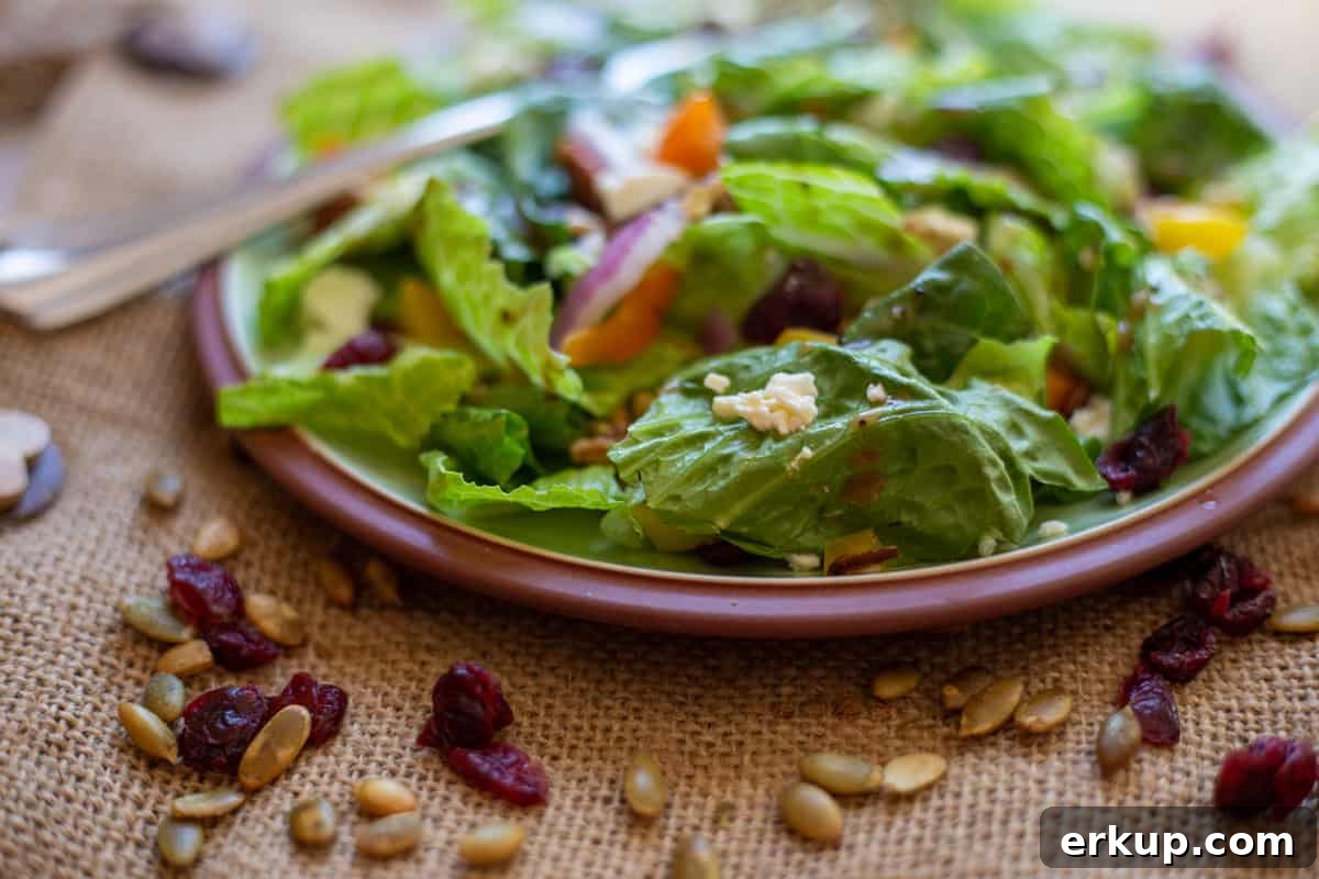 the salad on green plate with fork and dried cranberries, pumpkins seeds scattered around the plate.