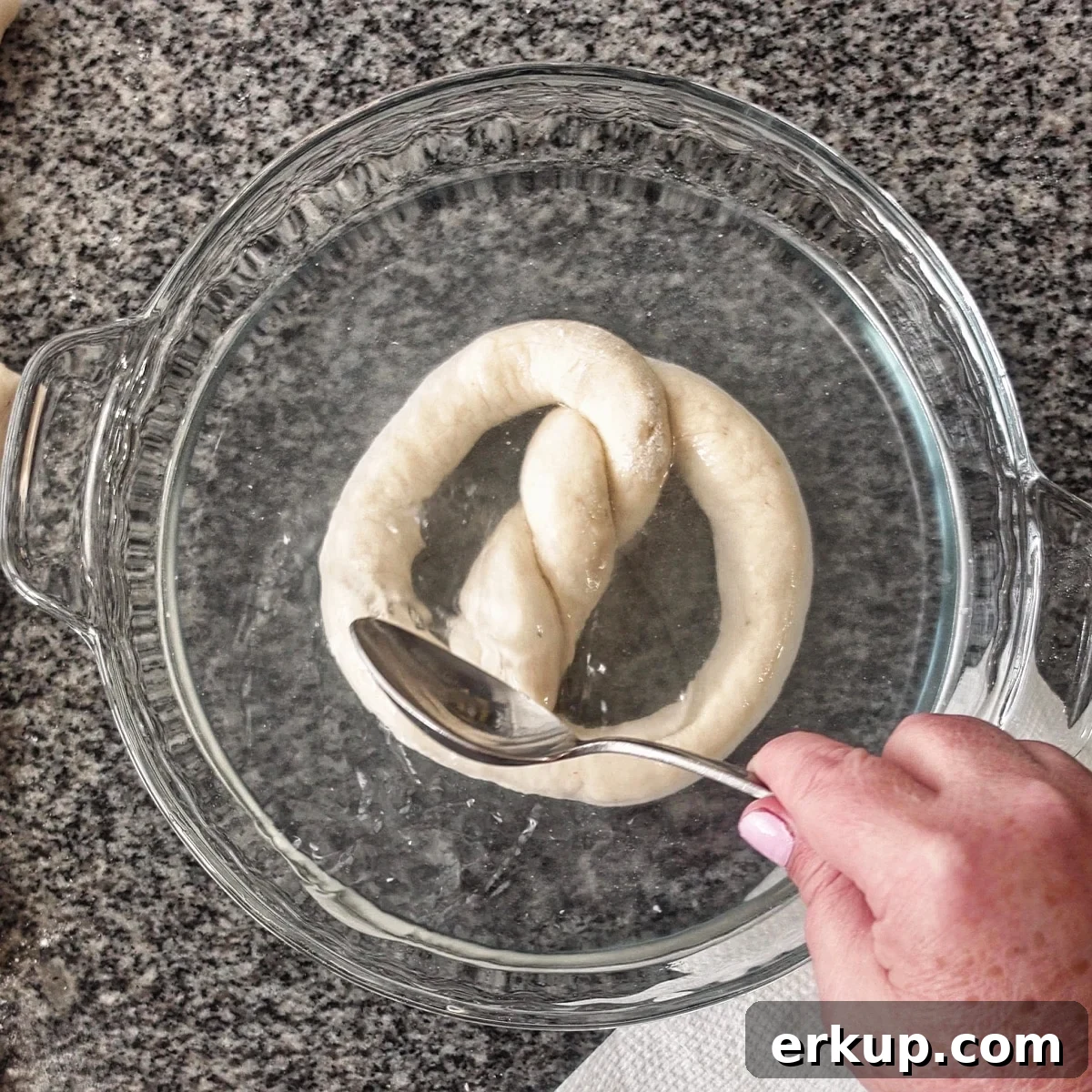 bathing pretzel in baking soda solution in glass pie plate.