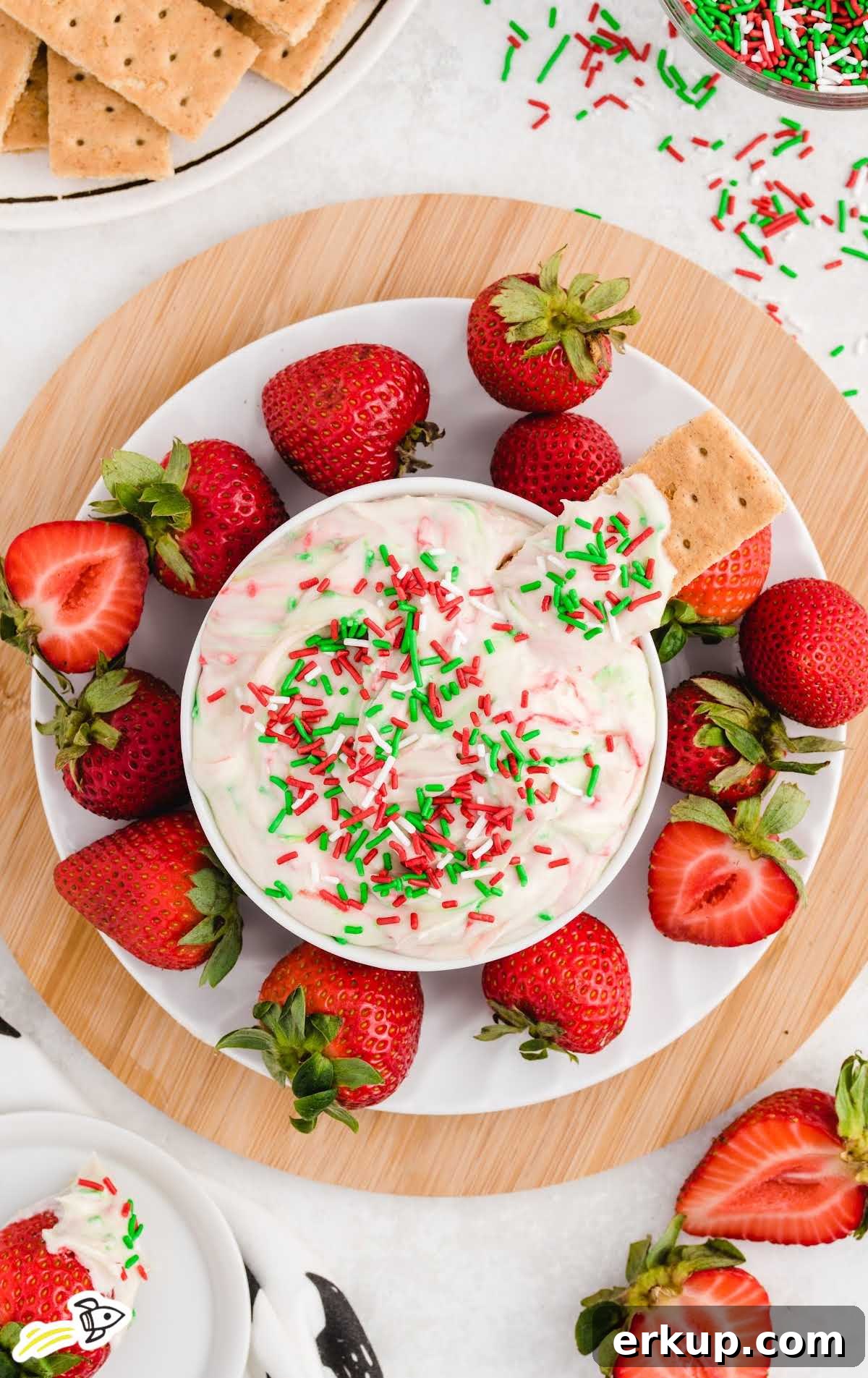 Creamy Christmas Sugar Cookie Dip Recipe for Holiday Parties 9 a close up shot of Christmas Sugar Cookie Dip in a bowl topped with a graham cracker with strawberries around it