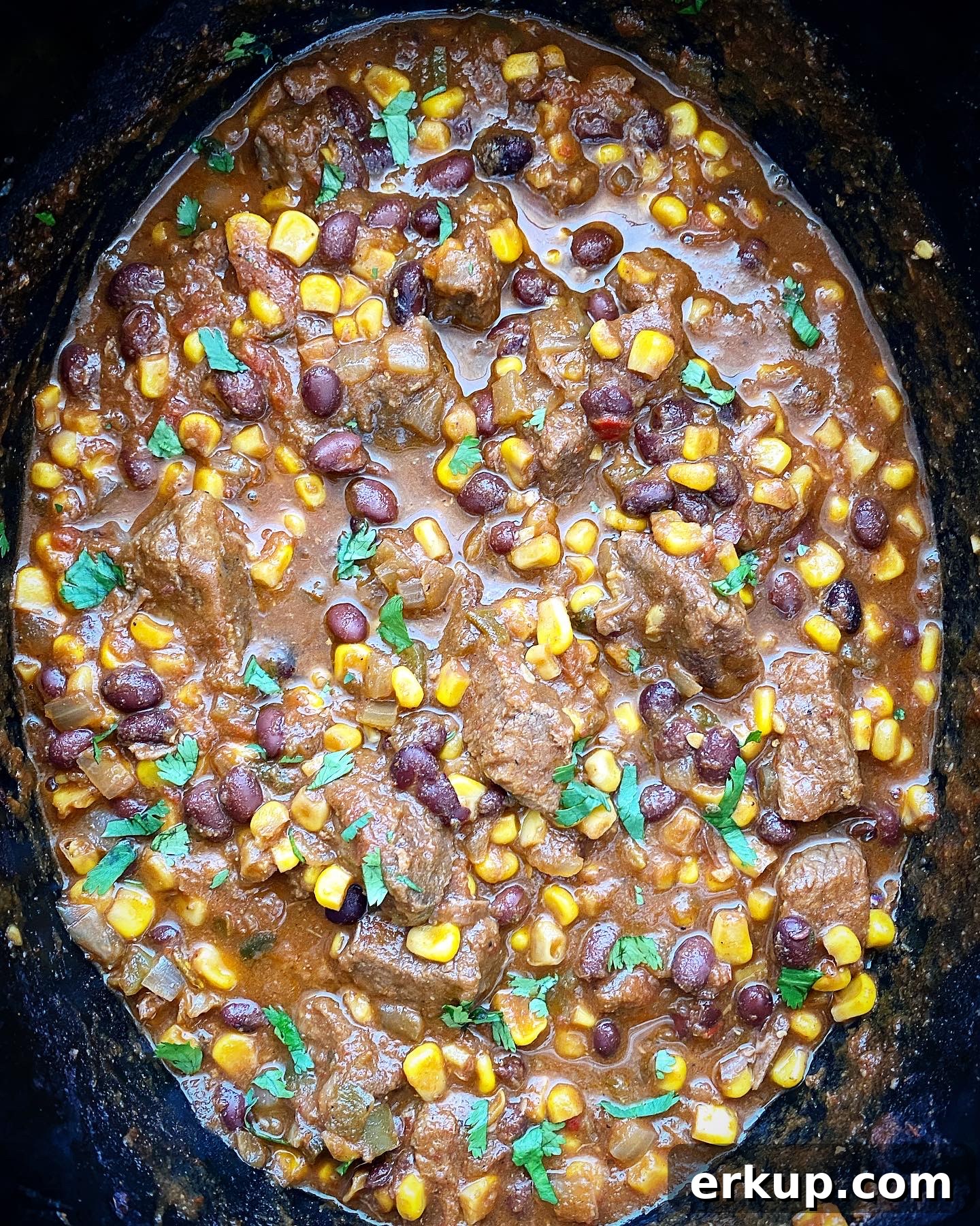 Slow Cooker Salsa Beef Stew Recipe 5 overhead shot of cooked salsa beef stew in a black slow cooker garnished with fresh cilantro