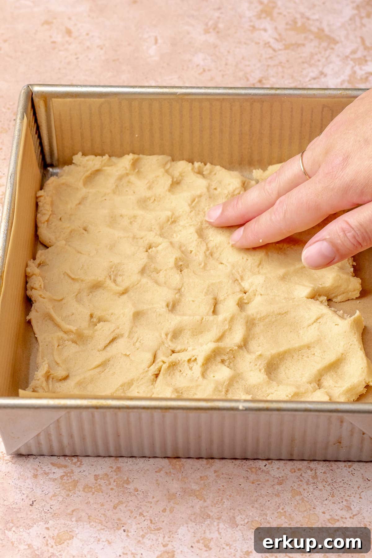 Pumpkin Pie Bars with Buttery Shortbread Crust 6 A hand presses shortbread dough into a square pan.