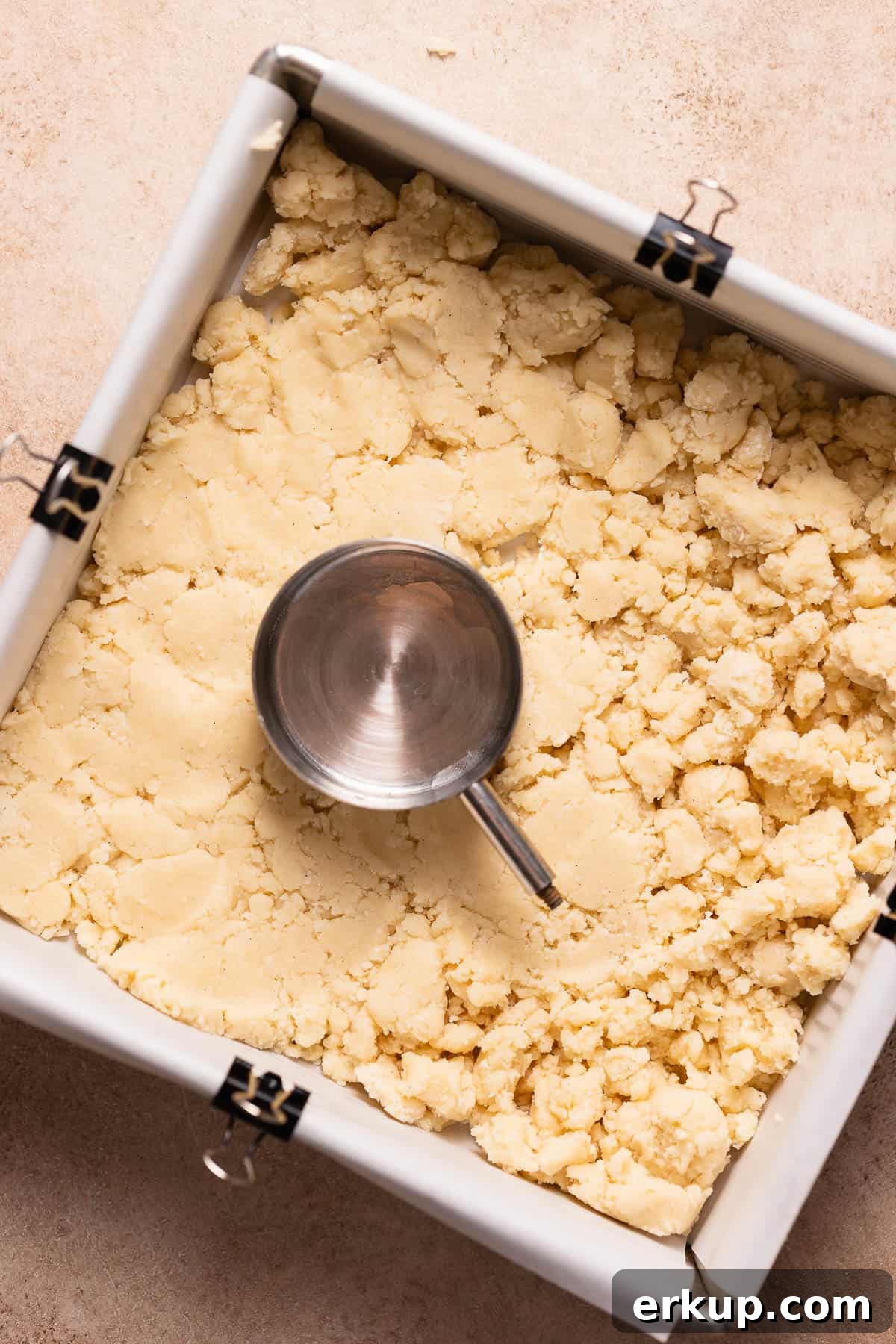 Shortbread crumbs being pressed into a baking pan.