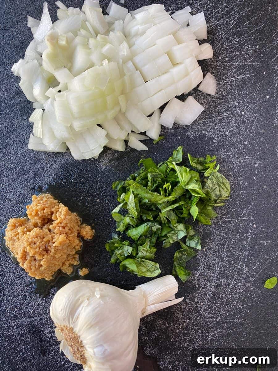 Creamy Cheesy Baked Ziti Casserole Recipe 3 Chopped onion, garlic and basil on a cutting board.