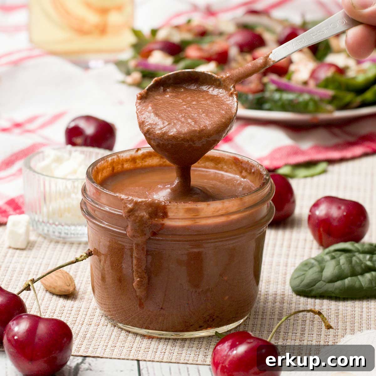 A spoon full of cherry balsamic vinaigrette with fresh cherries.