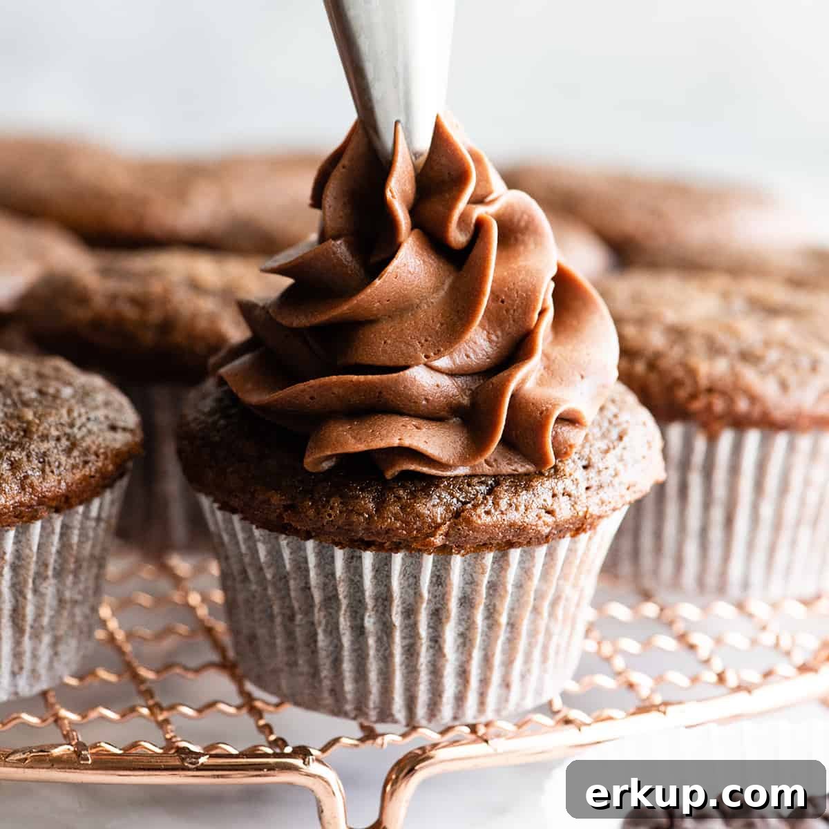 front photo showing frosting being piped onto a chocolate cupcake