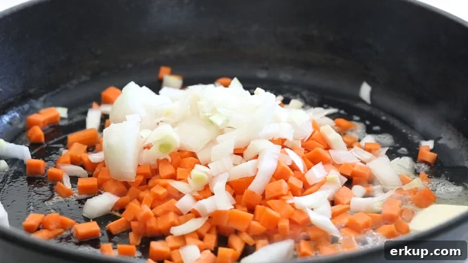 adding onions and carrots to a large cast iron skillet
